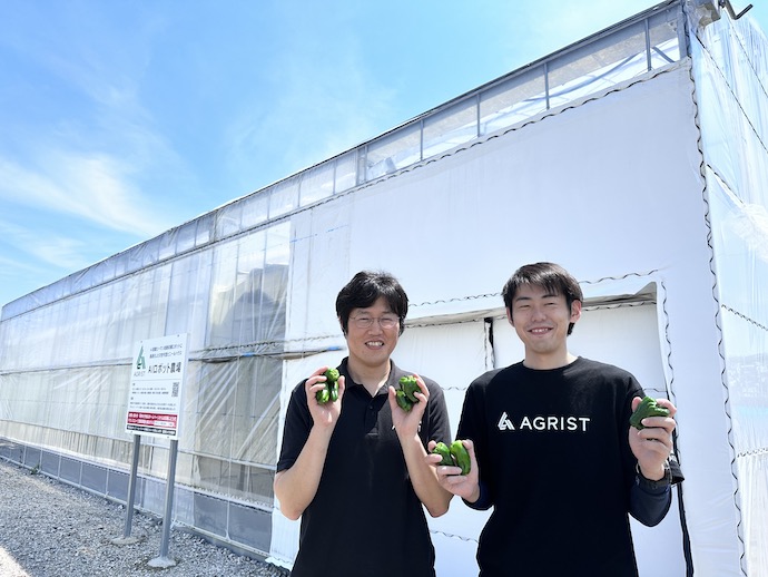 AGRIST株式会社の「AIロボット農場」の前に立つ農場管理者2名