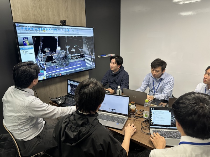 アイサンテクノロジー株式会社のメンバーが大型ビジョンを見ながらミーティングをしている様子