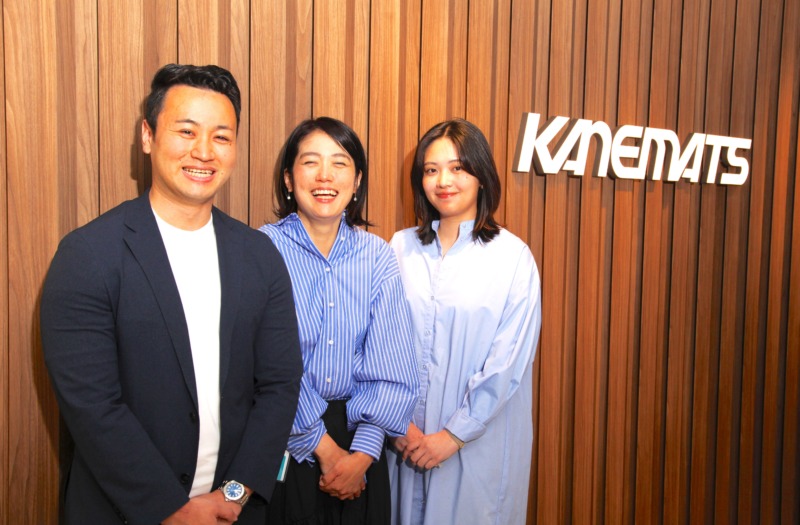 会社ロゴの前で笑顔を浮かべる兼松株式会社の社員3名