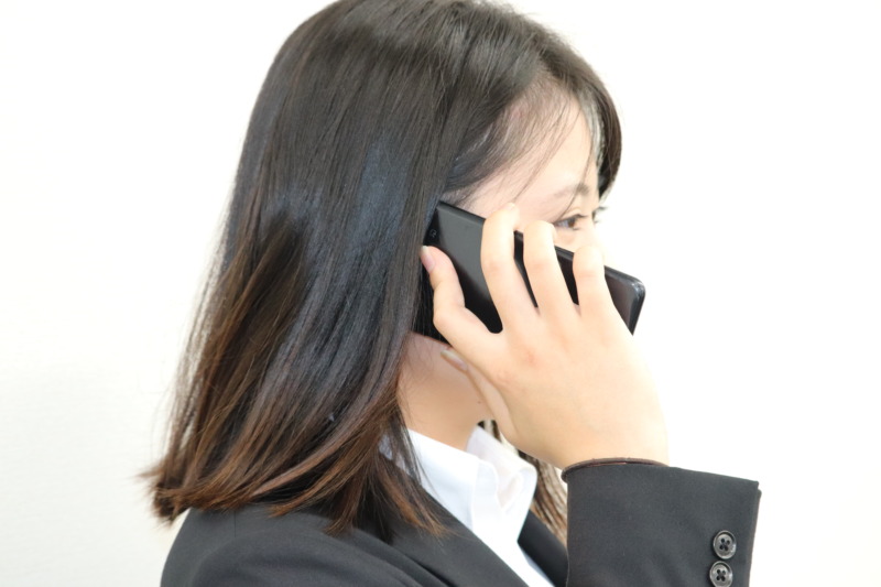 携帯電話で通話中の松阪興産株式会社の女性社員