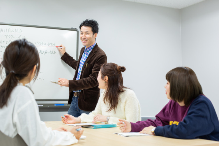 株式会社オリンピアの社内ミーティングで女性3名が男性上司から説明を受けている様子