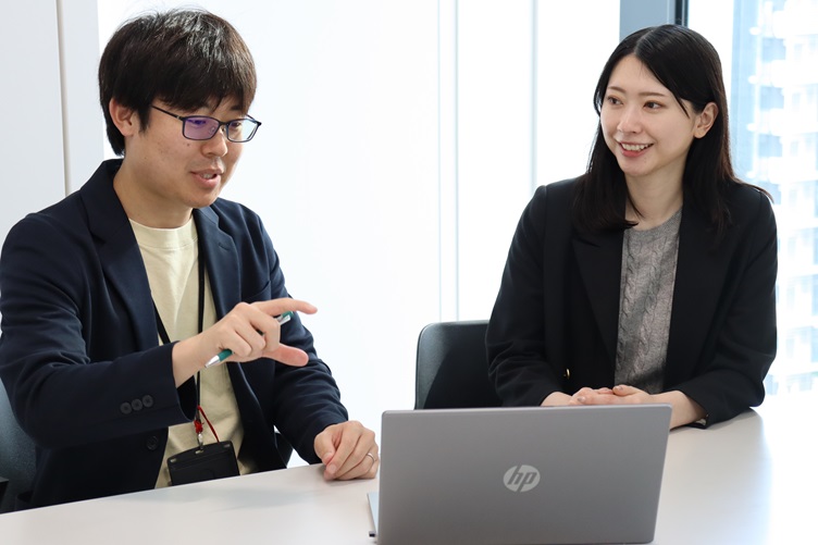 六元素情報システム株式会社の管理本部で人事採用担当をしている奥村龍太郎さんと古川みくさんがPCに向かって談笑している様子 その1
