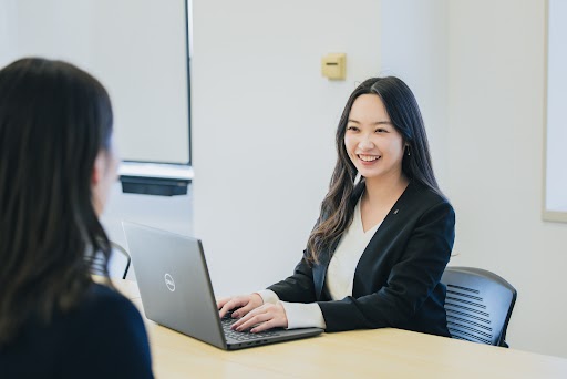 タカマツハウス株式会社のPCに向かう女性社員が対面の人物と笑いながら作業している様子