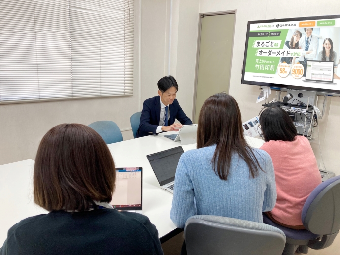 竹田印刷株式会社の中村本部長が、若手と共に働いている様子